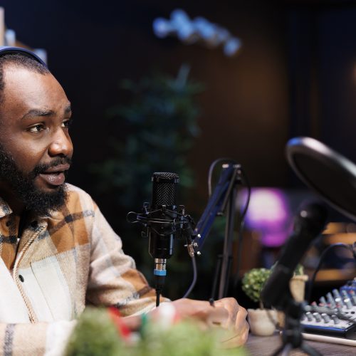 Man talk show host using audio equipment and having a friendly interview with an upcoming artist at home studio. African american content creator with headphones and microphone is creating a podcast.